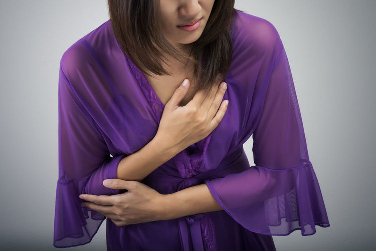 Midsection of woman with chest pain against gray background