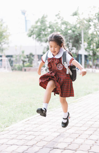 Full length of schoolgirl jumping at paving stones