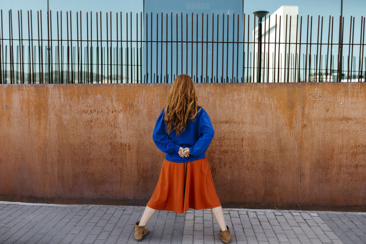 Rear view of woman standing with legs apart while facing wall