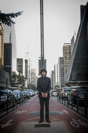 Full length portrait of young man standing against buildings in city