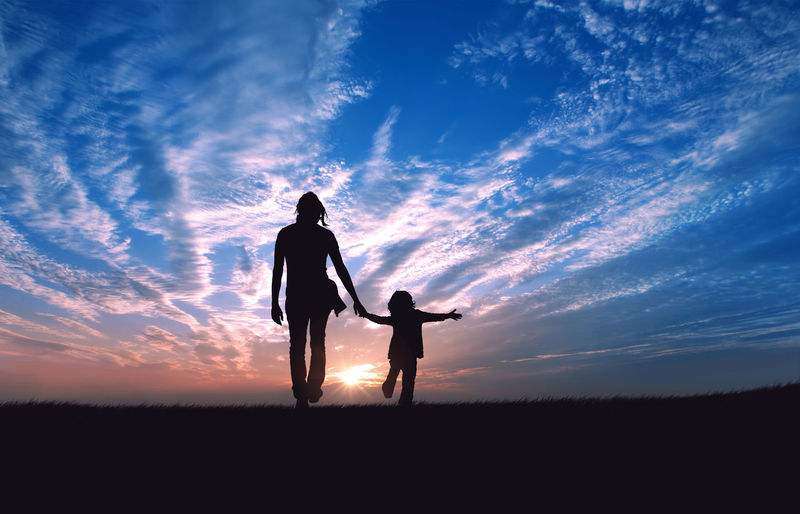 Silhouette of father and son standing on field at sunset