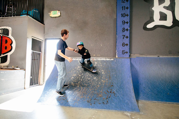 Skateboard instructor holds the hand of student while he is on ramp