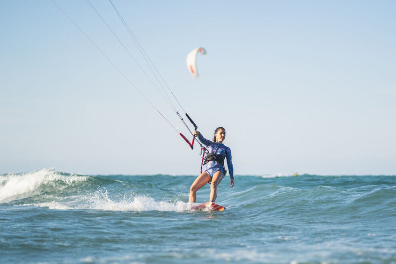 Fit female kite surfer in swimsuit ridding waves in sea on sunny day in summer
