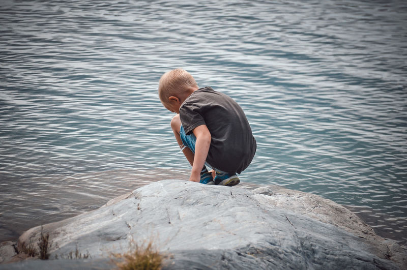 Rear view of boy on rock by lake