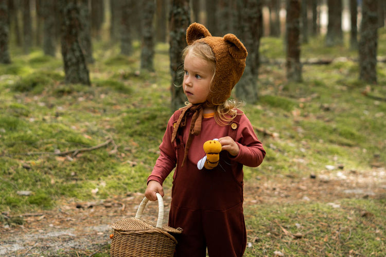 Toddler baby girl in bear bonnet walking in the woods