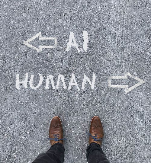Man looking down at the words artificial intelligence - ai - and human chalked onto the floor
