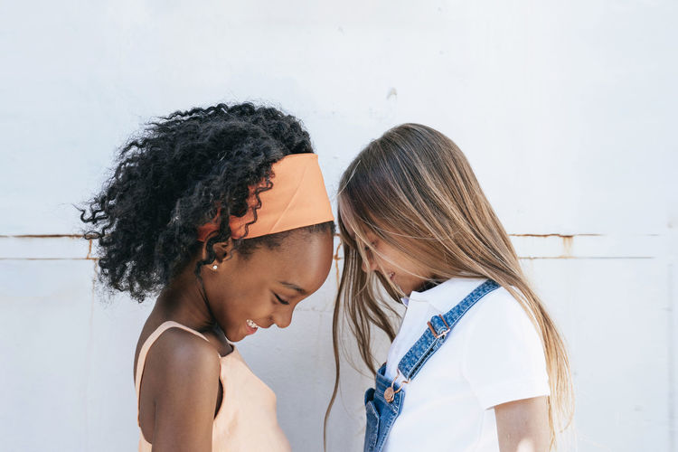 Cheerful african american girl with best friend having fun near white wall