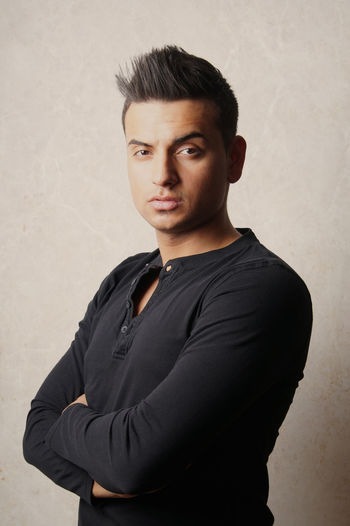 Portrait of confident young man with arms crossed standing against wall