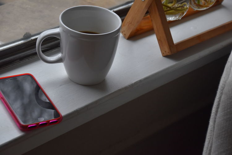 Close-up of coffee and cellphone on window ledge 