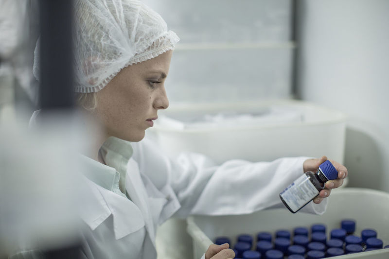 Lab worker in pharmaceutical plant looking at pill bottle