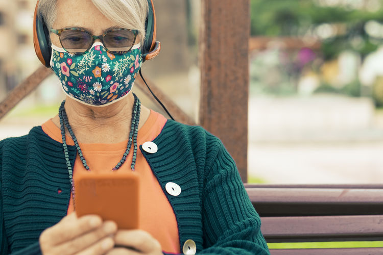 Senior woman wearing mask using smart phone outdoors