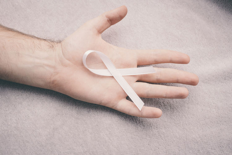 Cropped hand of man holding breast cancer awareness ribbon over bed