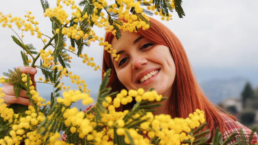 Portrait of young woman standing by yellow flowering plant