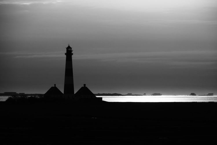 Silhouette of building by sea against sky