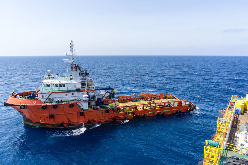 An anchor handling tug boat maneuvering near a construction work barge at offshore oil field