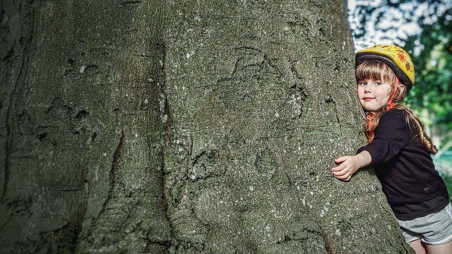 Portrait of cute girl embracing tree trunk