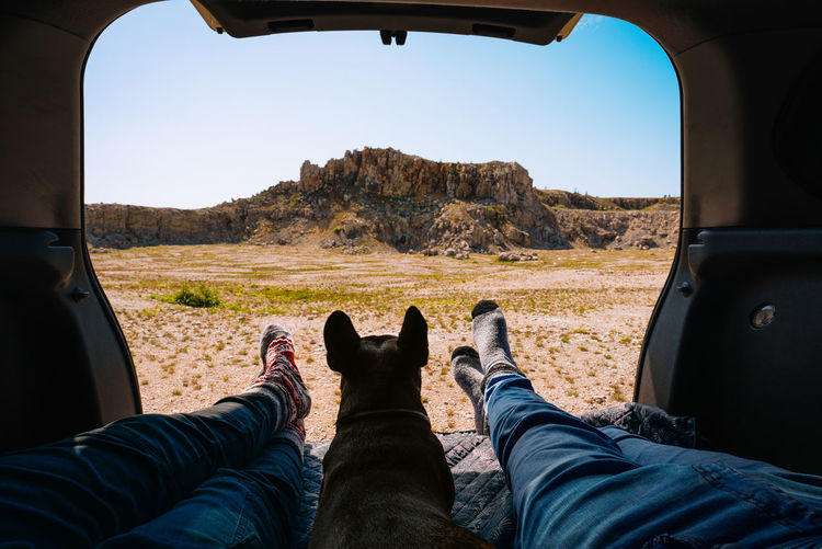 Low section of man and woman sitting in car trunk with french bulldog dog against mountains. travel. 