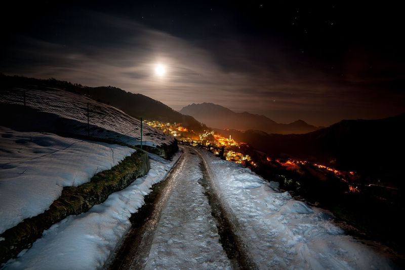 Snowy mountain village at night with the moon