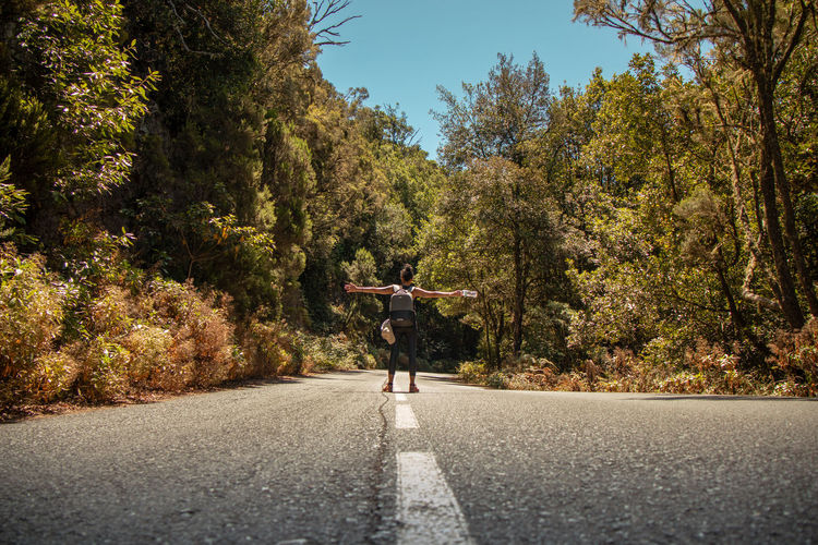 Rear view of person on road amidst trees during autumn