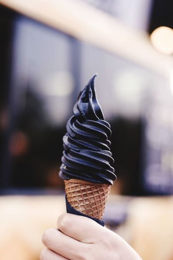 Cropped hand holding ice cream cone against bus