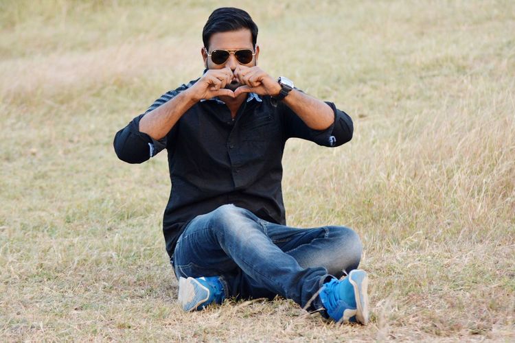 Man wearing sunglasses making heart shape while sitting on land