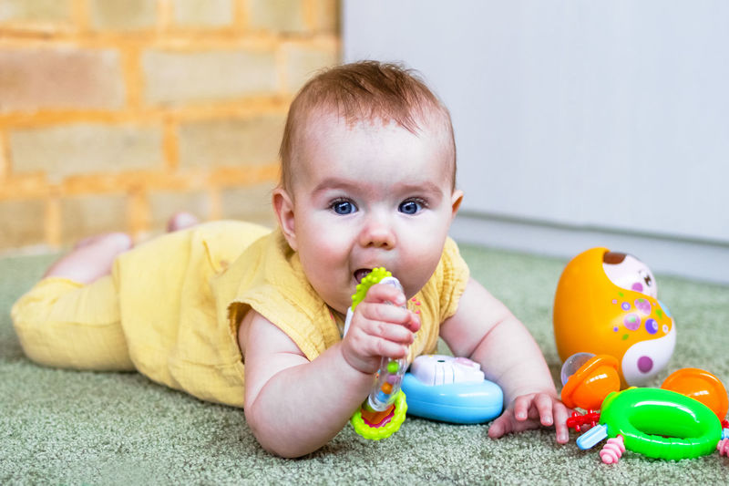 Little baby girl lying on a floor and playing with colorful toys. develop of child motor skills.