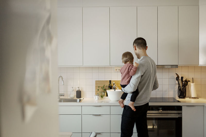 Father carrying toddler girl in kitchen