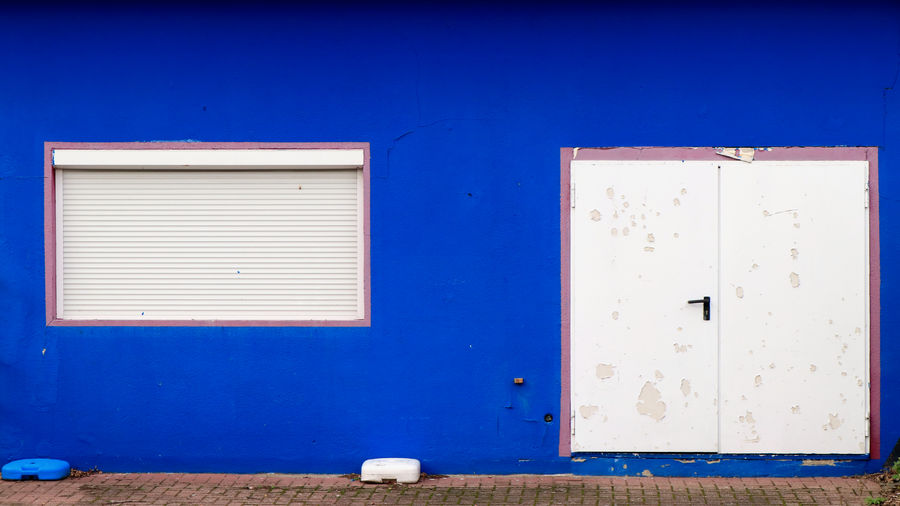 Blue house wall with white door and white closed roller shutter