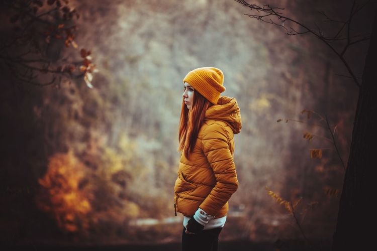 Side view of young woman standing in forest during autumn