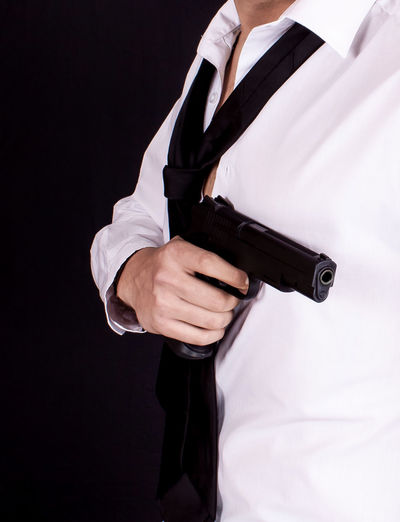 Midsection of man with handgun standing against black background