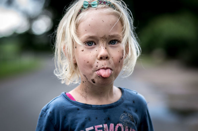 Portrait of cute girl with messy face sticking out tongue