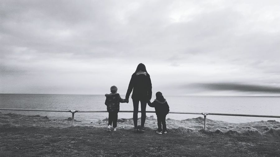 Rear view of mother with sons standing at beach against sky