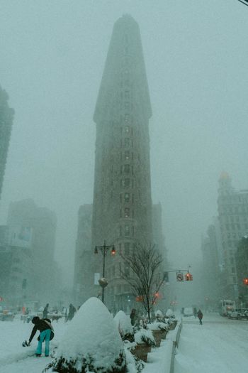 Person in snow covered city against sky during foggy weather