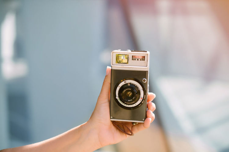 Crop hand of young woman holding portable analog photo camera against blurred background