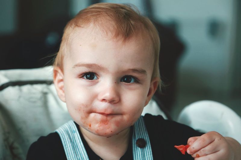 Close-up portrait of cute baby boy eating food while sitting at home
