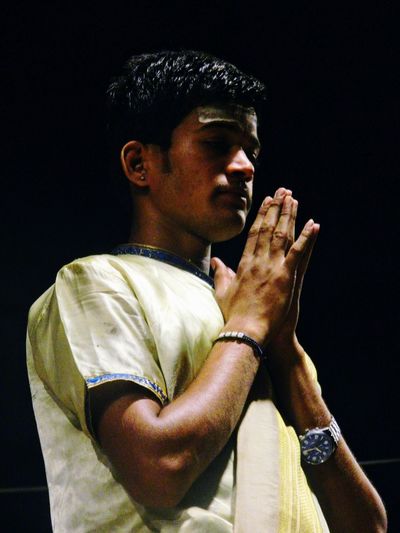 Low angle view of young man praying while standing against sky at night