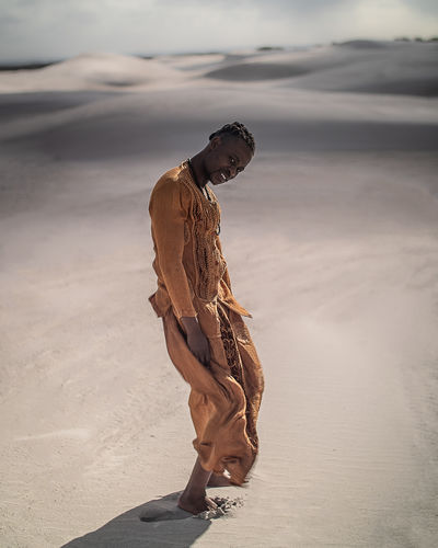 Full length portrait of young man wearing traditional clothing standing at desert