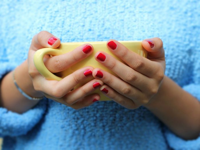 Midsection of woman with red nail polish holding yellow cup