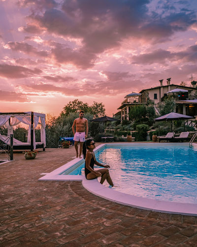 Woman sitting on swimming pool against sky during sunset