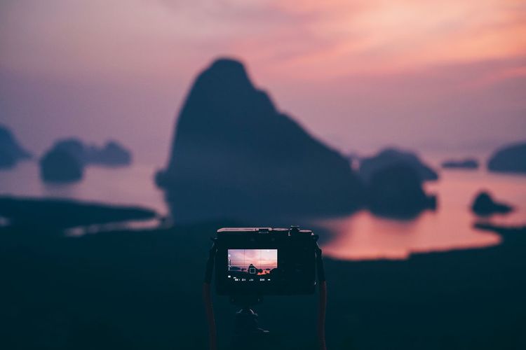 Close-up of camera photographing against sky during sunset