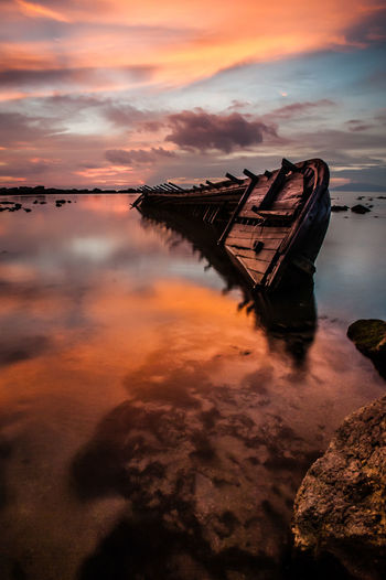 Abandoned boat in sea against sky during sunset