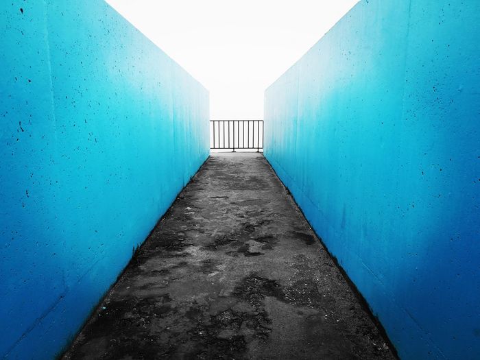 Empty footpath amidst blue walls against sky
