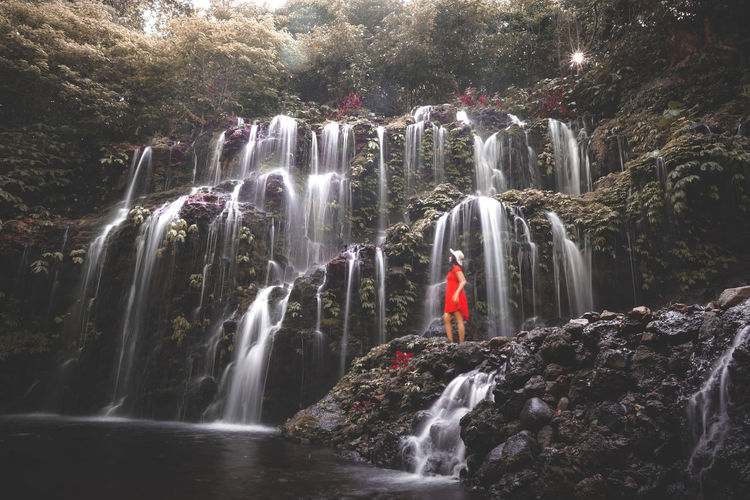 Woman standing on rock formation by waterfall in forest