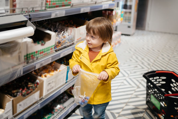 Child in the market with a grocery cart, puts sweets in a bag