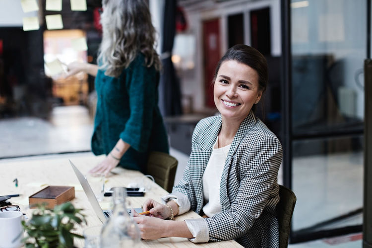 Portrait of smiling businesswoman sitting by female colleague at meeting in office