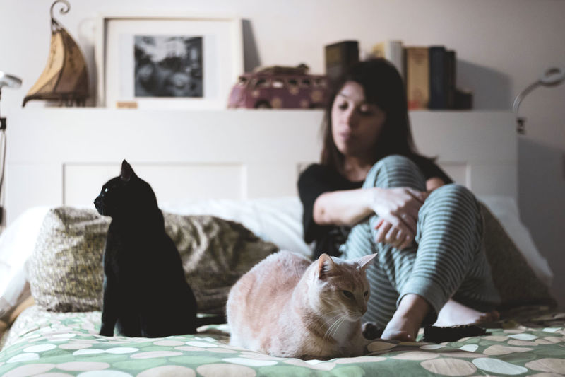 Woman with cats sitting on bed at home