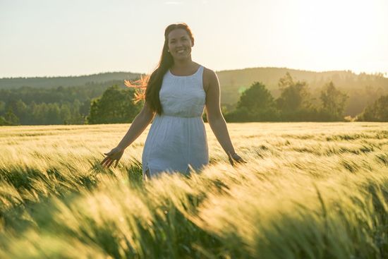 Smiling woman walking amidst grassy field against sky on sunny day