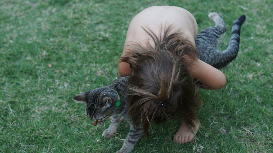 High angle view of shirtless girl hugging her pet cat on field