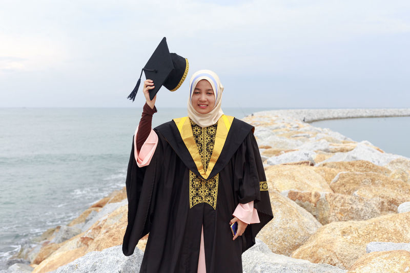 Young woman wearing graduation gown on groyne at sea