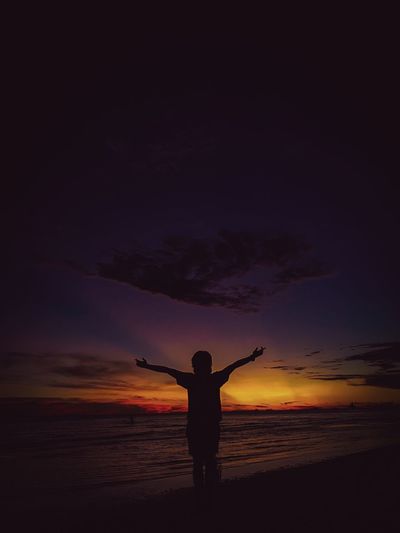 Silhouette person standing on shore against sky during sunset